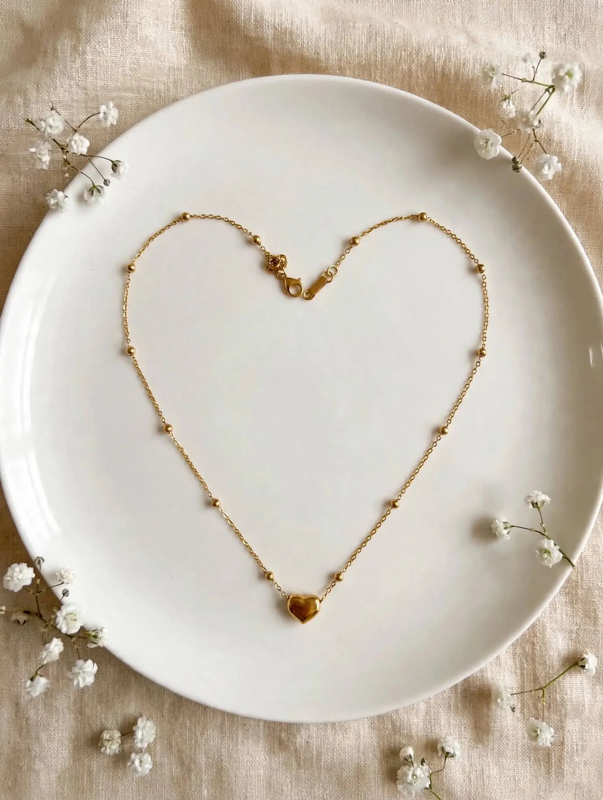 Gold heart beaded necklace in heart shape on white plate